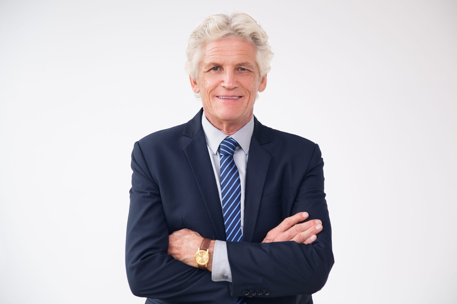 Studio portrait of senior Caucasian businessman wearing suit standing with folded arms, looking at camera and smiling